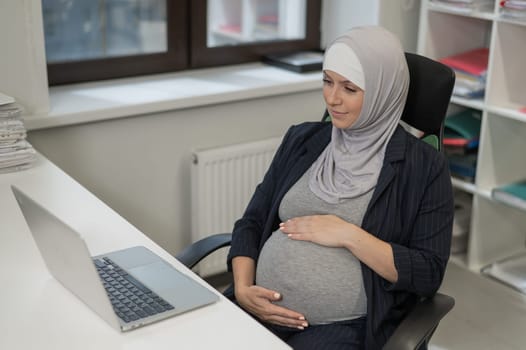 Pregnant Caucasian woman in hijab working at a computer in the office