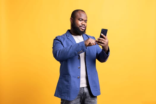 Man scrolling on smartphone touchscreen, using mobile phone to check social media feed. African american person browsing internet websites, isolated over studio background