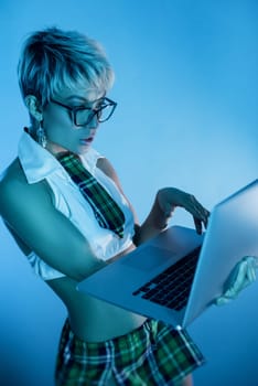 Sexy girl in glasses and an erotic school suit with a plaid skirt with a laptop in blue neon light on the background of copy paste