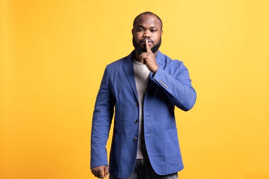 Annoyed african american man doing shushing hand gesturing, irritated by noise, having negative mood. Person placing finger on lips, doing quiet sign gesture, studio background