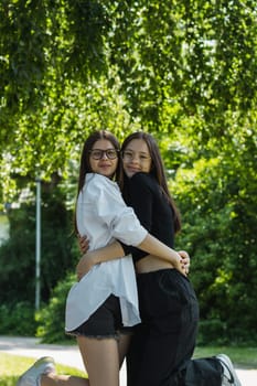 Portrait of two young beautiful Caucasian girls hugging and looking at the camera in a city park on a summer day, bottom view.