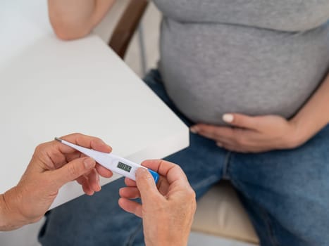 A pregnant woman visits a doctor. Therapist holding an electronic thermometer