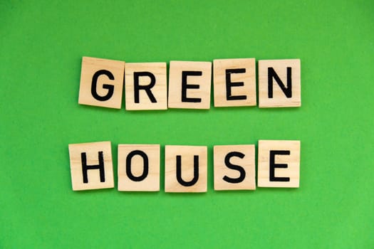 Green house text on wooden blocks on green background. Ecological concept Sustainable responsible living. Copy space. Single word