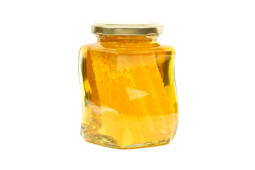 A glass jar with a golden lid contains honey with honeycomb filled almost to the top, against a white background