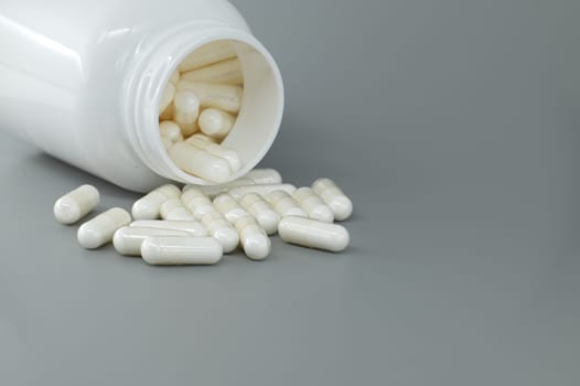 Overturned white medicine bottle with its contents white pills or capsules, spilled out onto a gray background. Medical environment, pharmacy or a medical facility