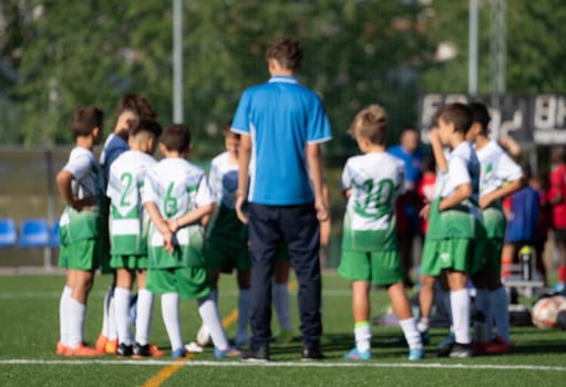 A group of young soccer players are huddled together on a field, with a coach watching over them