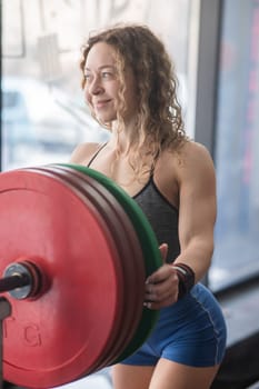 Caucasian forty year old woman putting a weight plate on a barbell in the gym. Vertical photo
