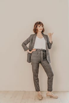 Brunette suit wall. Business woman in a beige suit posing on a beige background. Full length studio portrait