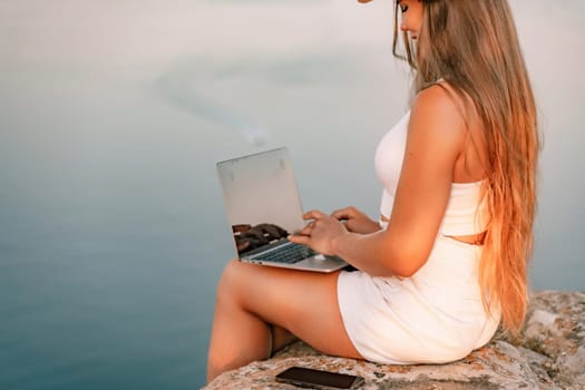 Freelance women sea working on the computer. Good looking middle aged woman typing on a laptop keyboard outdoors with a beautiful sea view. The concept of remote work