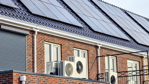 air source heat pump unit installed outdoors at a modern home with solar panels in the Netherlands, new house with black solar panels. Zonnepanelen, Zonne energie, Translation: Solar panel, Sun Energy