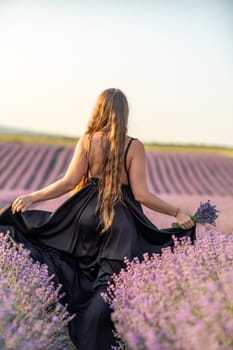 A woman in a black dress is walking through a field of lavender. The field is purple and the sky is blue