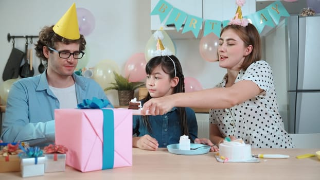 Caucasian mother cutting cake while family congratulate in girl's birthday. Diverse family celebrate daughter important day while waiting for eating dessert and food while smiling together. Pedagogy.