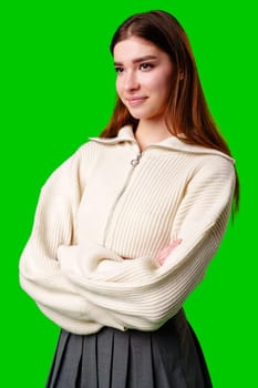 A young woman stands confidently against a vivid green background, dressed in a casual yet fashionable white cropped hoodie and a gray pleated skirt. Her expression is serene with a hint of contemplation, and her body language exudes a relaxed poise.