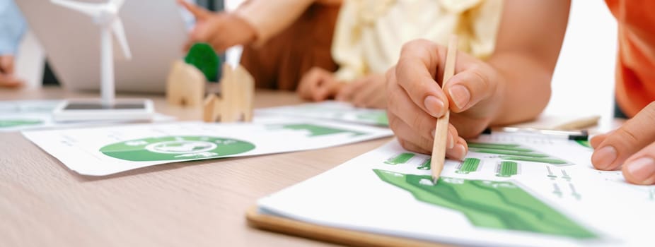 Windmill model represented using renewable energy placed during presenting green business on table with wooden block and environmental document scatter around. Closeup. Delineation.