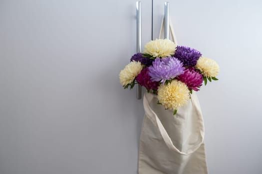 Mixed colorful flowers in cotton bag on door knob. Creative minimalistic flowers. Concept of holiday celebrating present and gift. Bouquet delivery Copy space