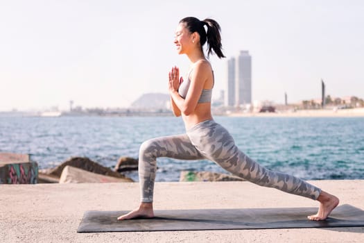 smiling young asian woman in sportswear practicing yoga by the sea, relaxation and healthy lifestyle concept