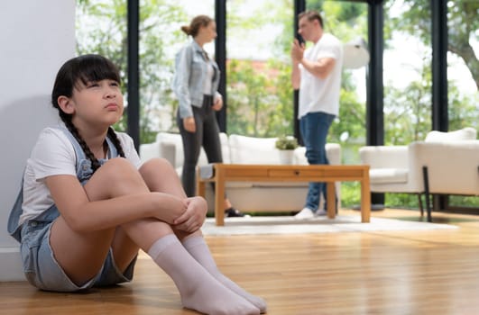 Stressed and unhappy young girl huddle in corner crying and sad while her parent arguing in background. Domestic violence at home and traumatic childhood develop to depression. Synchronos