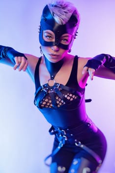 A sexy girl in the erotic image of a catwoman in leather bdsm straps and a mask poses against a copy paste background on beautiful neon background