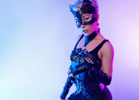 A sexy girl in the erotic image of a catwoman in leather bdsm straps and a mask poses against a copy paste background on beautiful neon background