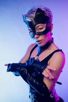 A sexy girl in the erotic image of a catwoman in leather bdsm straps and a mask poses against a copy paste background on beautiful neon background