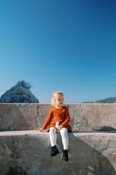 Little girl sits on a stone bench on an observation deck by the sea. High quality photo