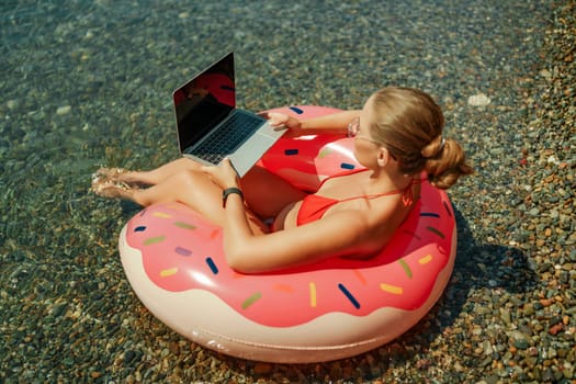 Woman laptop sea. Freelancer woman in sunglases floating on an inflatable big pink donut with a laptop in the sea. People summer vacation rest lifestyle concept