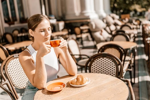 Portrait of happy woman sitting in a cafe outdoor drinking coffee. Woman while relaxing in cafe at table on street, dressed in a white T-shirt and jeans.