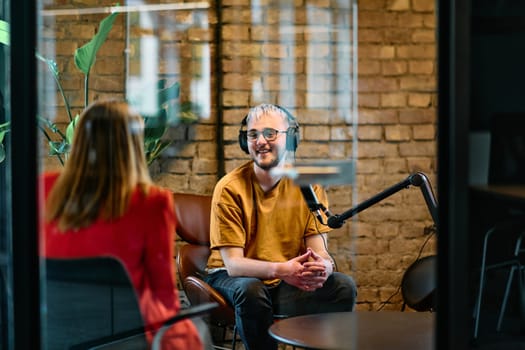 A gathering of young business professionals, some seated in a glass-walled office, engage in a lively conversation and record an online podcast, embodying modern collaboration and dynamic interaction.