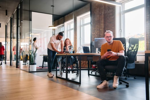 A diverse group of business professionals collaborates in a modern startup coworking center, utilizing a mix of paper-based and technological tools such as mobile phones and computers .