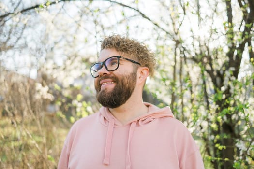Man with beard and mustache on smiling face near sakura flowers or blooming spring tree. Soft and gentle concept. Bearded man with stylish haircut with flowers on background, close up. Hipster near branch of bloom tree