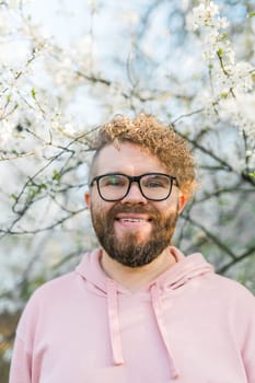 Man with beard and mustache on smiling face near sakura flowers or blooming spring tree. Soft and gentle concept. Bearded man with stylish haircut with flowers on background, close up. Hipster near branch of bloom tree