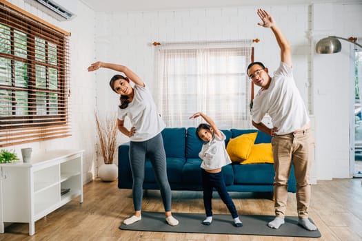 In their domestic setting Asian parents and their daughter enjoy a harmonious family weekend while practicing yoga and fitness training promoting health and education.