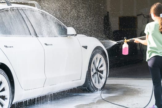 Denver, Colorado, USA-September 1, 2023-A young girl enthusiastically assists in washing the family's electric car in their suburban driveway.