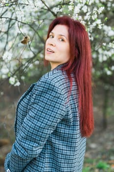 Beautiful happy millennial woman enjoying smell in a flowering spring garden. Blooming tree time.