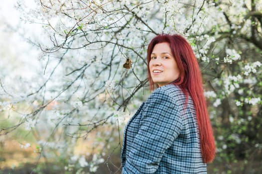 Beautiful happy millennial woman enjoying smell in a flowering spring garden. Blooming tree time.