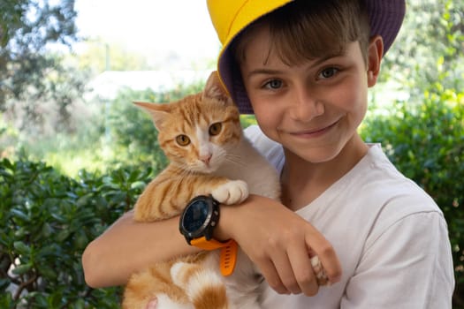 Cheerful boy in a yellow Panama hat with a red cat. High quality photo