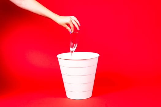 A woman is disposing of a cup in a trash can, making a gesture with her hand to pour out the liquid from the glass drinkware