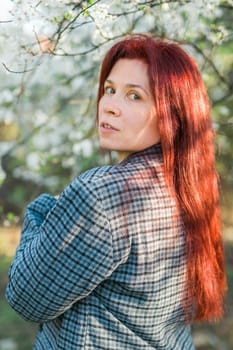 Beautiful young red hair woman near blooming spring trees alley. Youth and love, fashion and romantic and lifestyle concept