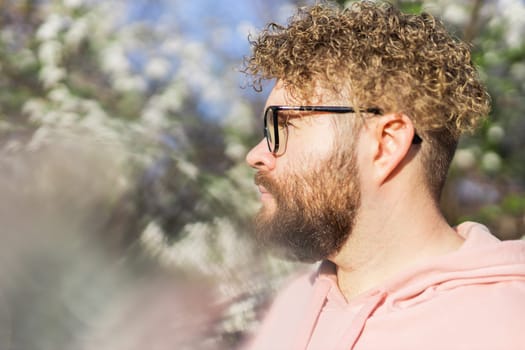 Cool handsome millennial man side face looking away portrait in blooming springtime trees. Blur sakura blossom spring tree background. Copy space.