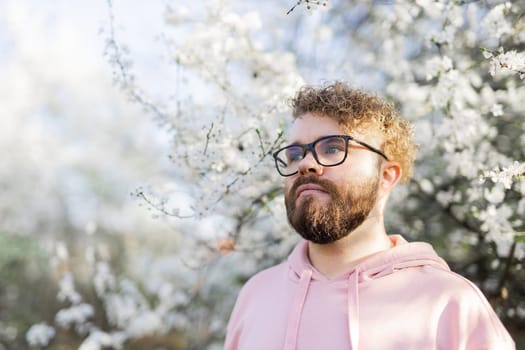 Cool handsome millennial man side face looking away portrait in blooming springtime trees. Blur sakura blossom spring tree background. Copy space.