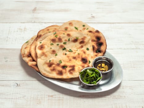 Fresh naan bread on white wooden background with copy space. Several perfect naan flatbreads over metal tray
