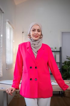 Confident Muslim businesswoman standing in front of desk in office.