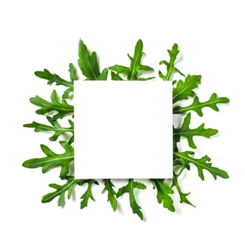 Creative layout made with arugula leaves. White paper square on heap of arugula or rucola leaves. Isolated on white with clipping path. Top view or flat lay. Copy space for text.