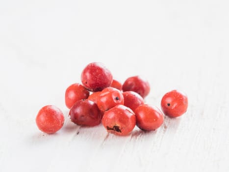 Heap of dried pink pepper berries on white wooden table. Close up view of pink peppercorn. Copy space.