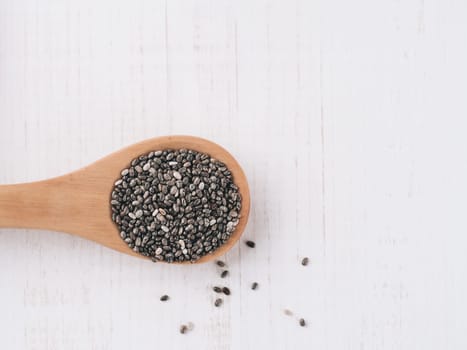 Dry chia seeds in wooden spoons on white wooden background. Cia seeds is superfood ingredient. Copy space for text.