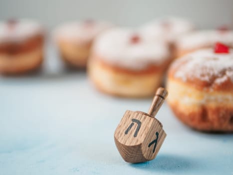 Jewish holiday Hanukkah concept and background. Hanukkah food doughnuts and traditional spinnig dreidl or dredel on blue background. Copy space for text. Shallow DOF