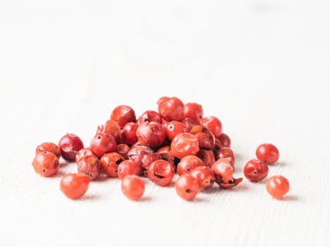 Heap of dried pink pepper berries on white wooden table. Close up view of pink peppercorn. Copy space.