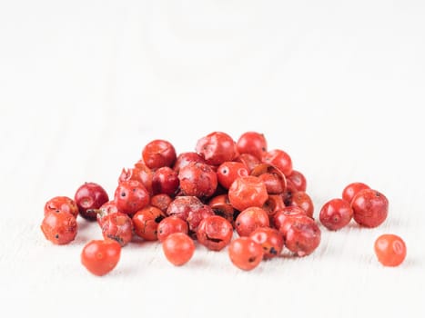 Heap of dried pink pepper berries on white wooden table. Close up view of pink peppercorn. Copy space.