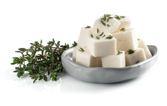 Diced soft cheese in rustic plate and fresh thyme isolated on white background with clipping path.