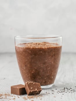 Chocolate chia pudding in glass and chocolate cubes slice on gray wooden table. Healthy vegan breakfast with copy space.